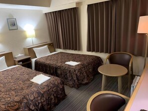 Ein Hotelzimmer mit zwei Betten, einem kleinen Tisch, einem Stuhl und einer Lampe.