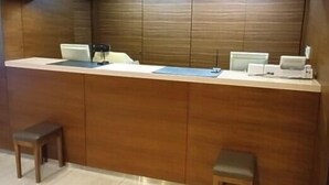 A reception desk with a wooden panel backdrop, a computer, and a telephone. There are two wooden stools and a small table with a chair. - Shizuoka Daiichi Hotel (Shizuoka)