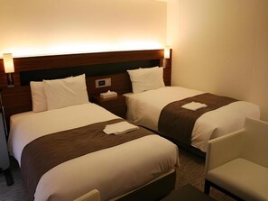 Ein Hotelzimmer mit zwei Betten, einem Nachttisch, einer Lampe und einem Sessel.