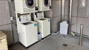 A laundry facility with two stacked dryers, a washing machine, and a trash bin. - Shizuoka Daiichi Hotel (Shizuoka)