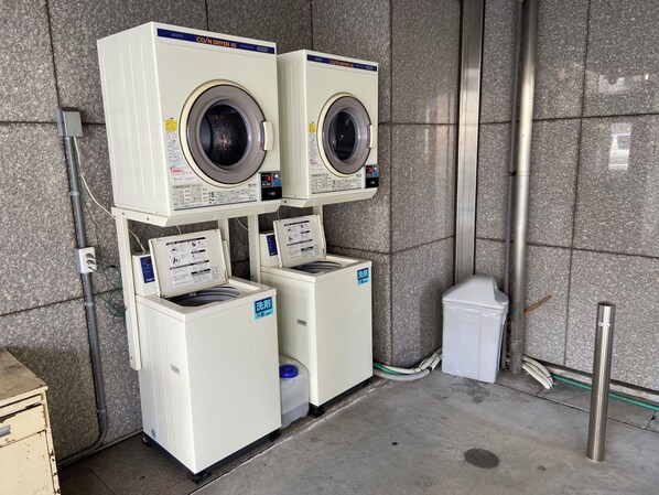 A laundry facility with two stacked dryers, a washing machine, and a trash bin. - Shizuoka Daiichi Hotel (Shizuoka)