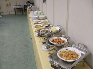 A buffet setup with various food items on trays and plates.