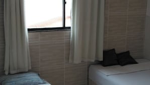 Een slaapkamer met een bed, een raam met gordijnen en een betegelde vloer.