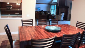 Uma área de refeições com mesa e cadeiras de madeira, um centro de mesa com tigela de vidro e uma cozinha ao fundo.