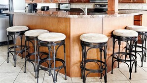 Cozinha com armários de madeira, uma ilha central com banquetas, micro-ondas e geladeira.