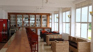 A bar area with a long wooden counter, wicker furniture, and a wall of liquor bottles. - Pulickal Airport Hotel (Entebbe)