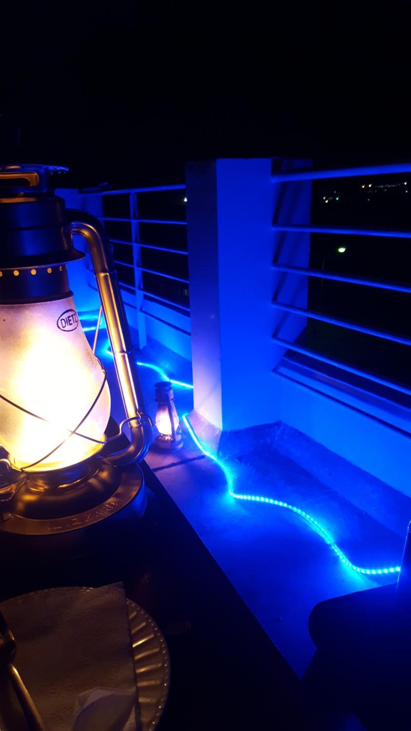 A lantern with a visible brand name, a window with horizontal blinds, and blue LED lights along the window frame.