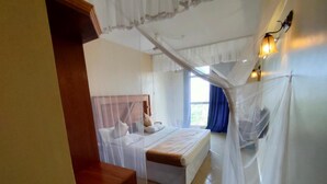 A bedroom with a bed under a mosquito net, a bedside table, and a window with curtains. - Pulickal Airport Hotel (Entebbe)