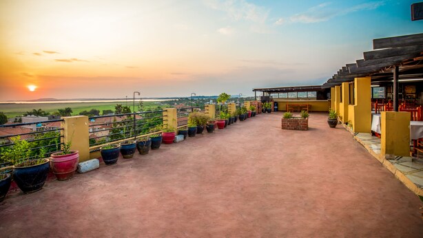 A rooftop terrace with potted plants, outdoor seating, and a view of the sunset. - Pulickal Airport Hotel (Entebbe)