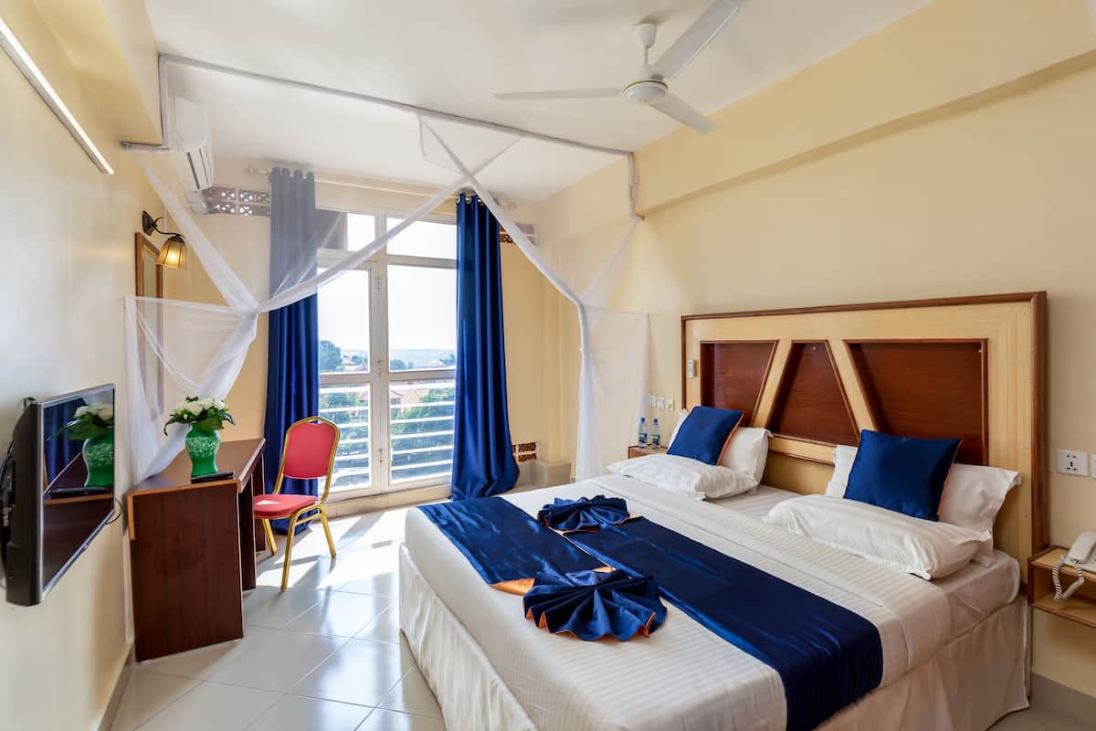 Quarto de hotel com uma cama grande, uma escrivaninha com cadeira, televisão e janela com cortinas.