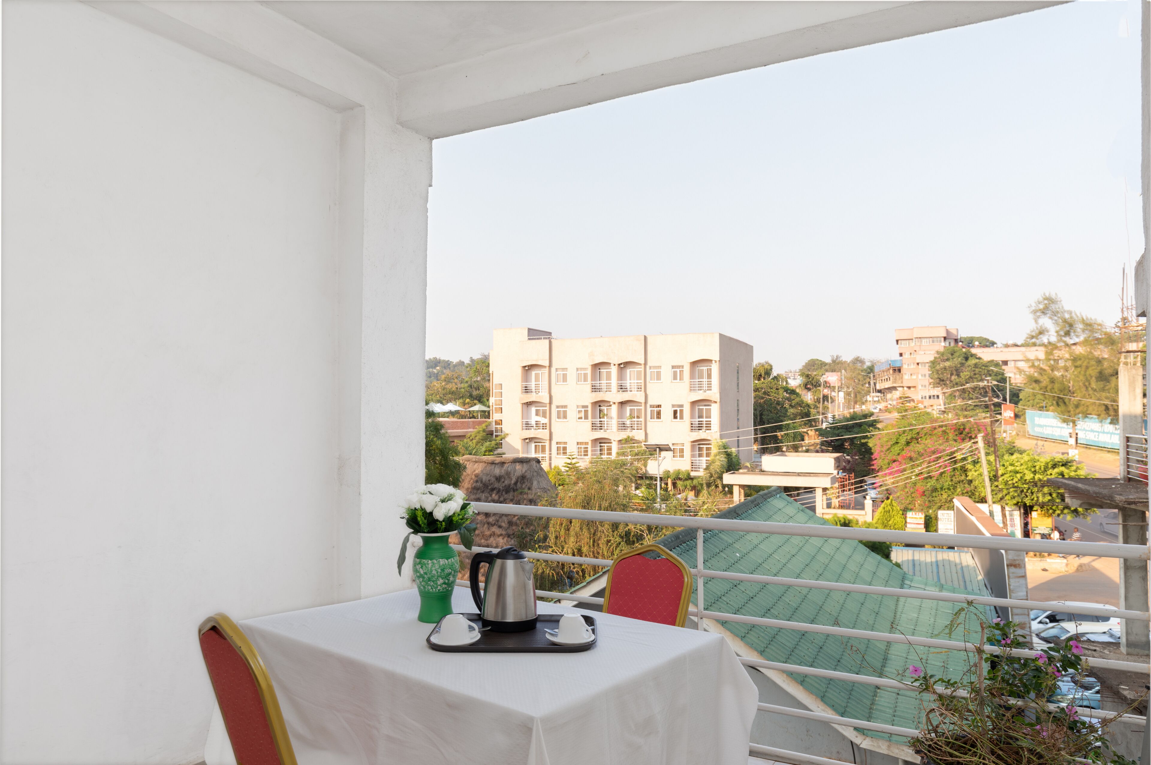 A balcony with a table set for two, a vase with flowers, and a kettle.