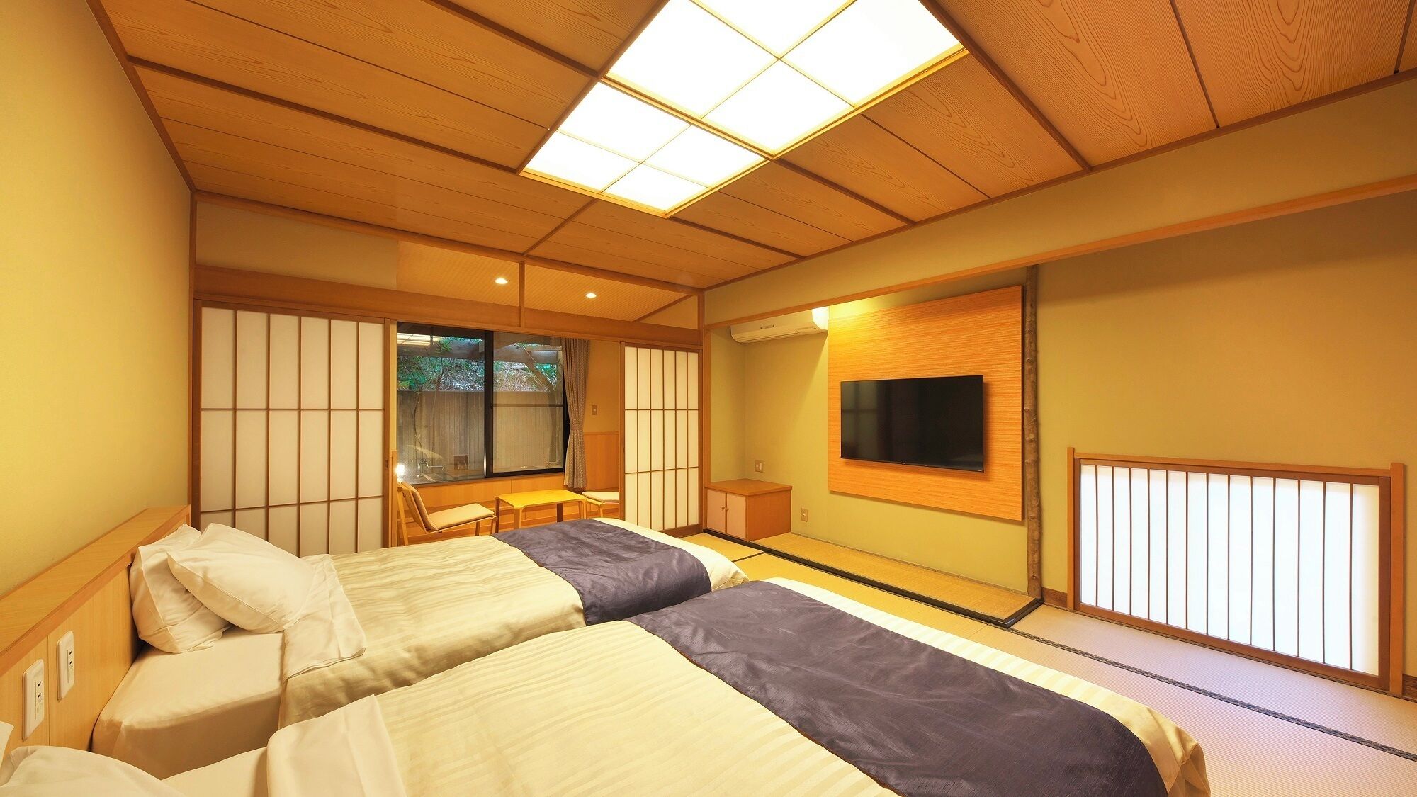 A traditional Japanese-style room with tatami flooring, a television mounted on the wall, and a sliding door leading to an outdoor area.