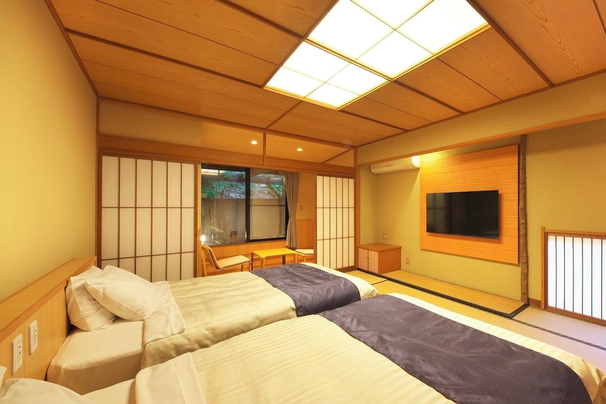 Una habitación tradicional japonesa con suelo de tatami, un televisor montado en la pared y una puerta corrediza que da a un espacio exterior.