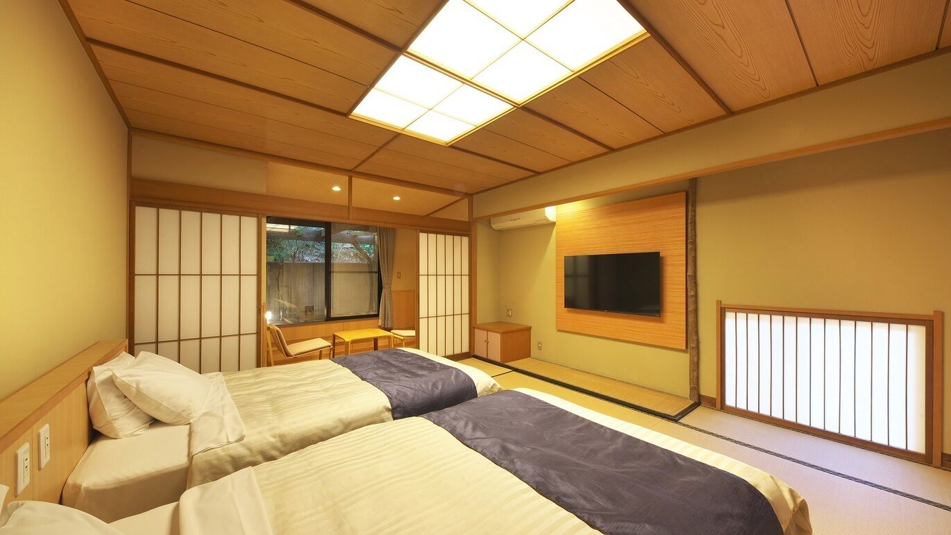 A traditional Japanese-style room with tatami flooring, a sliding door, a TV mounted on the wall, and a bed with a headboard.