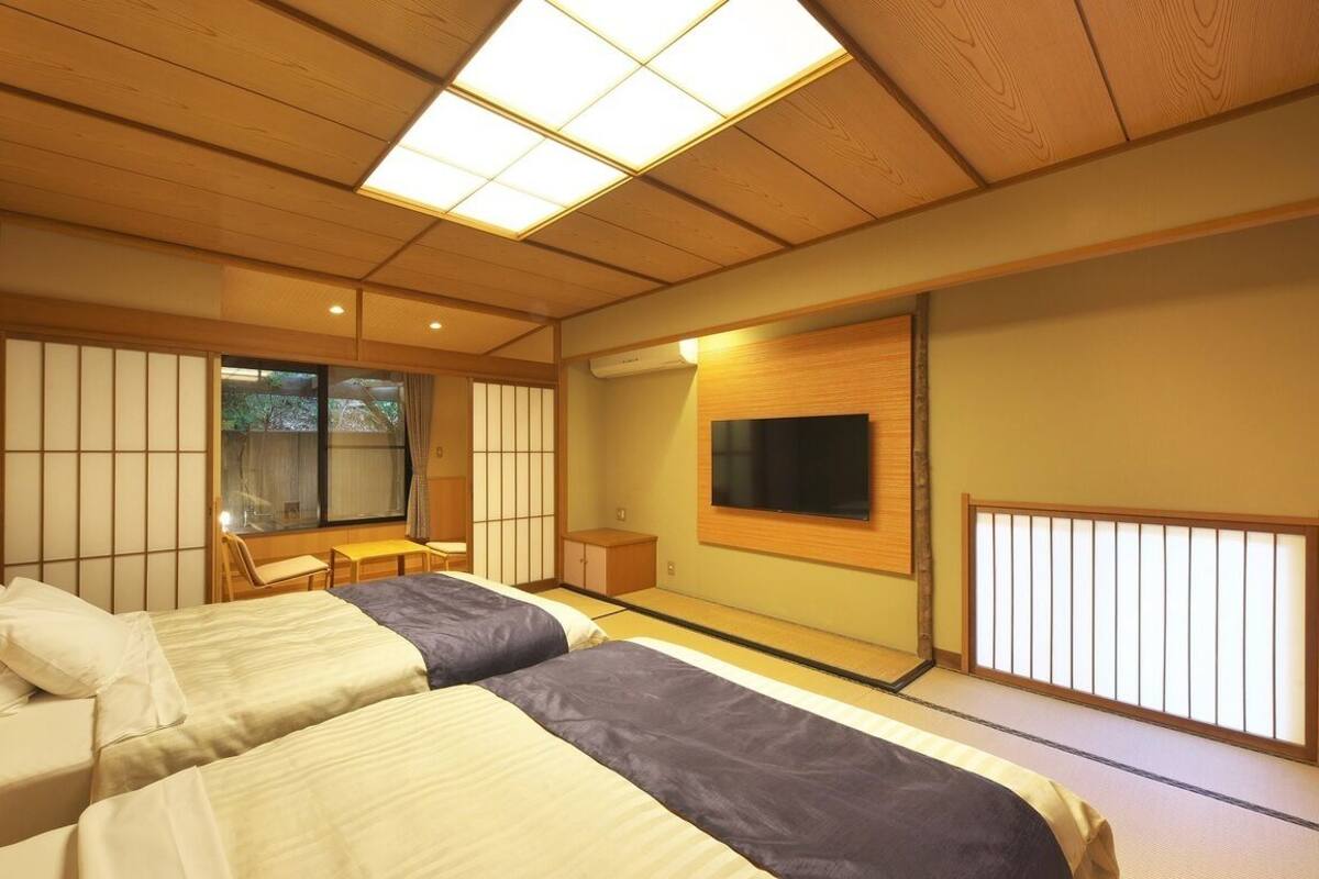Una habitación de estilo japonés tradicional con suelo de tatami, una puerta corredera, un televisor montado en la pared y una cama con cabecero.
