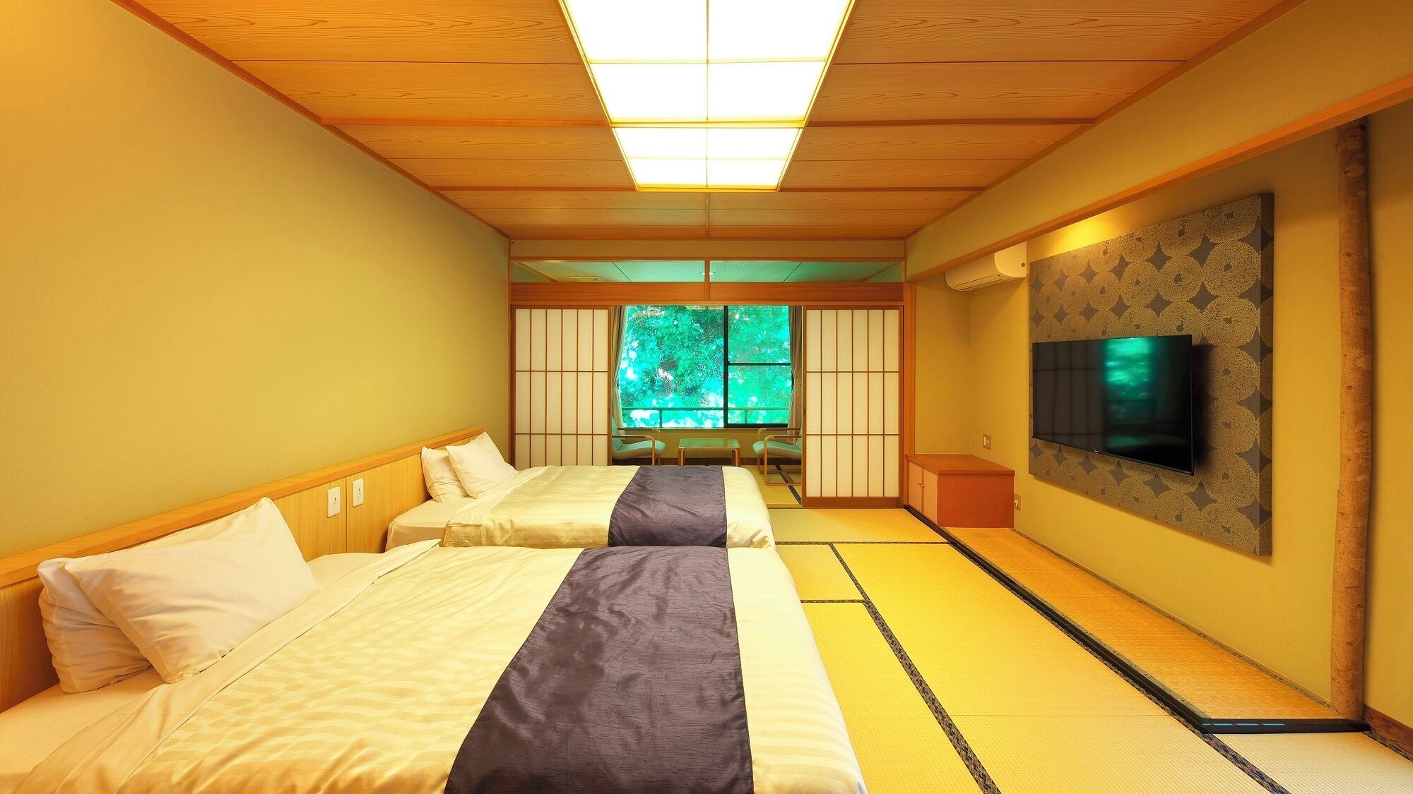 A hotel room with two beds, a TV, and a view of greenery through the window.