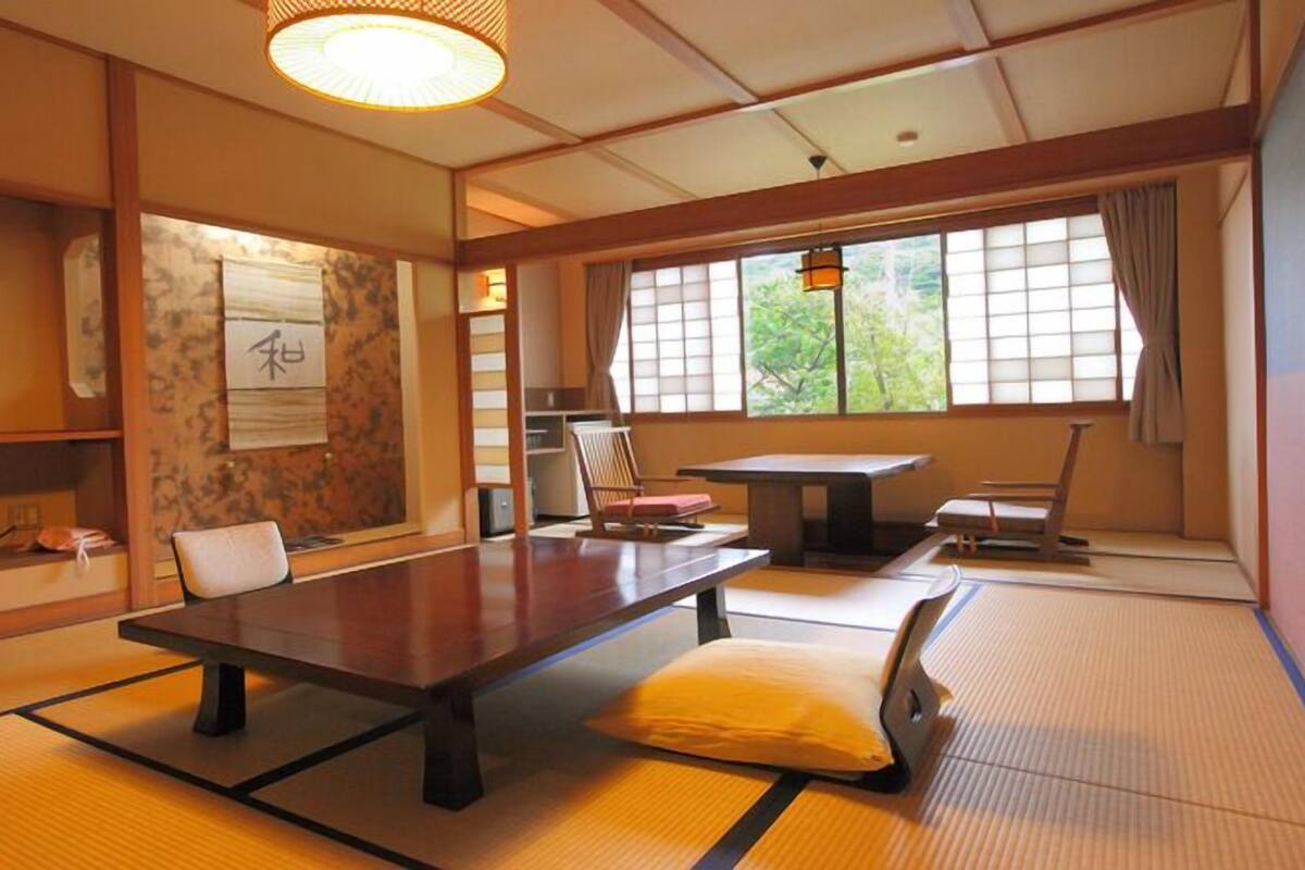 Una habitación tradicional japonesa con suelo de tatami, una mesa baja, sillas y un televisor.