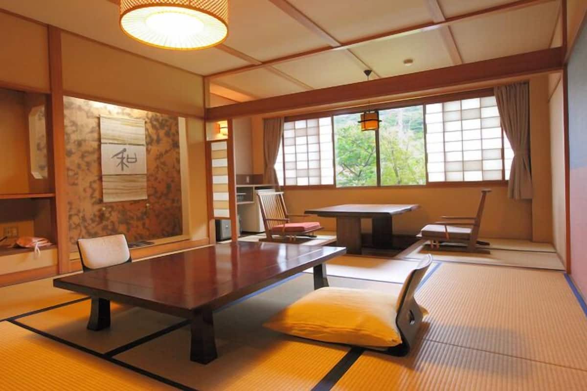 A traditional Japanese room with tatami flooring, a low table, chairs, and a television.