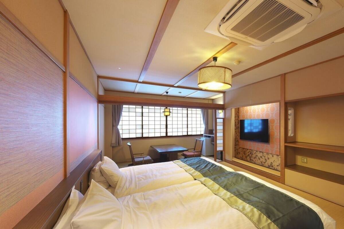 Una habitación de hotel con una cama, televisión, escritorio y ventana.