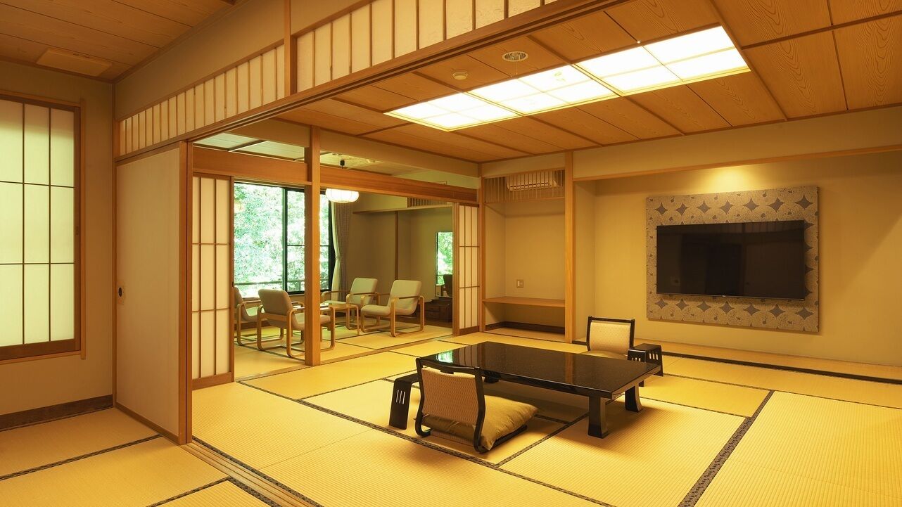 A tatami mat room with a tatami mat table, sliding doors, a television, and a view of the outdoors.