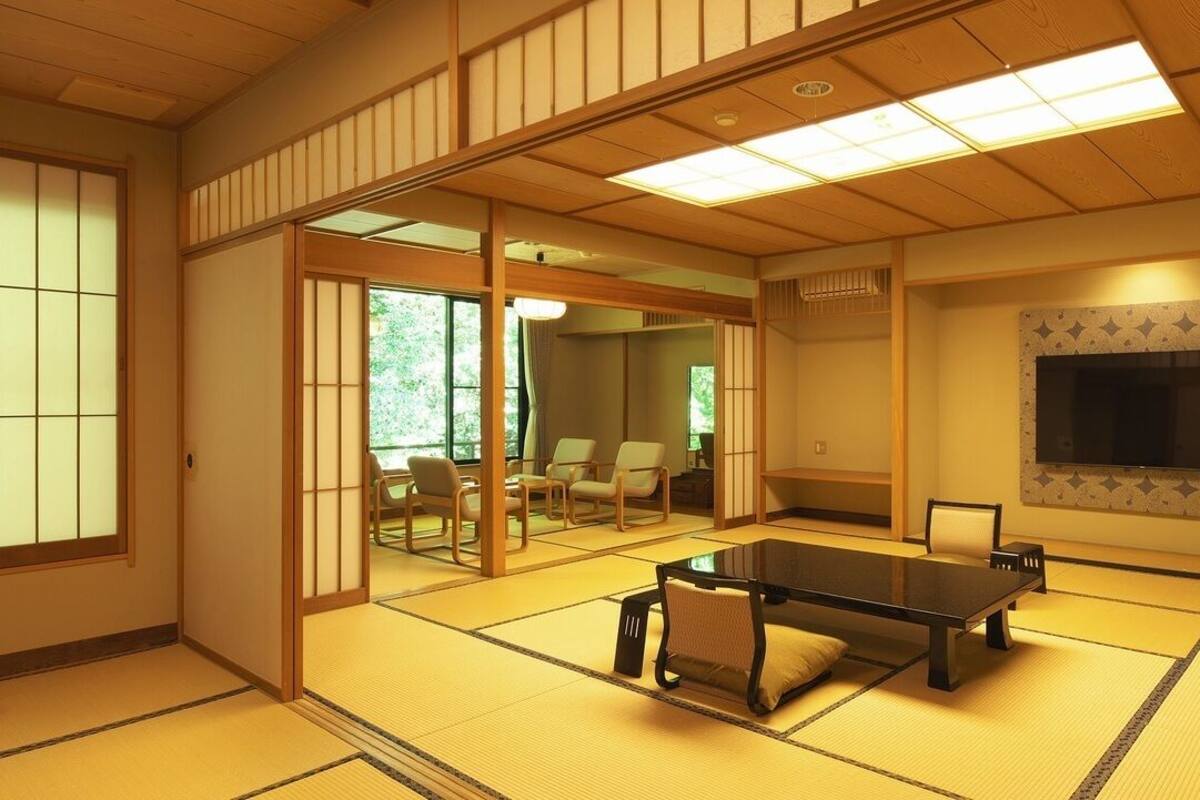 Una habitación con esteras de tatami, una mesa de tatami, puertas correderas, un televisor y vistas al exterior.