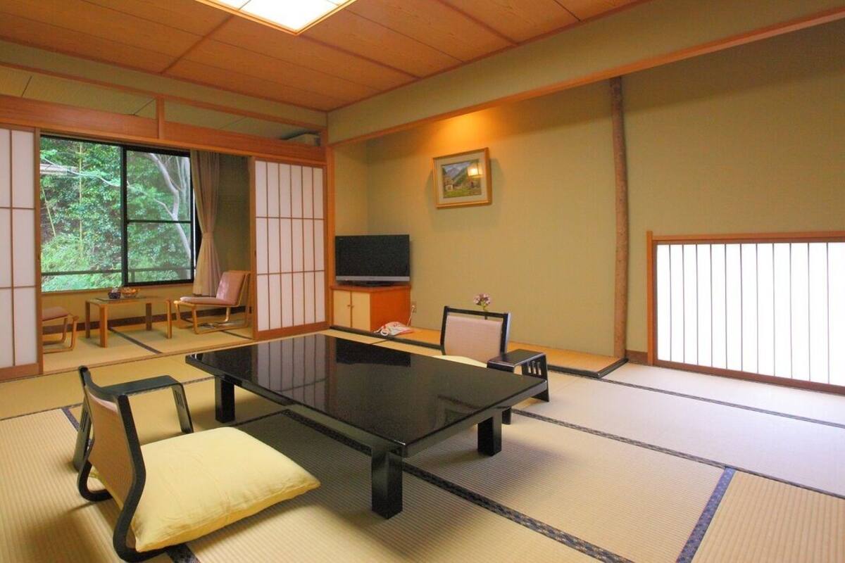 Una habitación japonesa tradicional con suelo de tatami, una mesa baja, sillas, un televisor y una puerta corredera.
