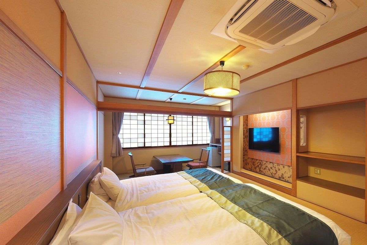 Una habitación de hotel con cama, escritorio, televisor y ventana con cortinas.
