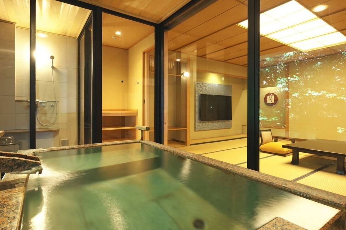 Un interior moderno con una amplia piscina interior, suelo de madera y una zona de estar con mesas y sillas.