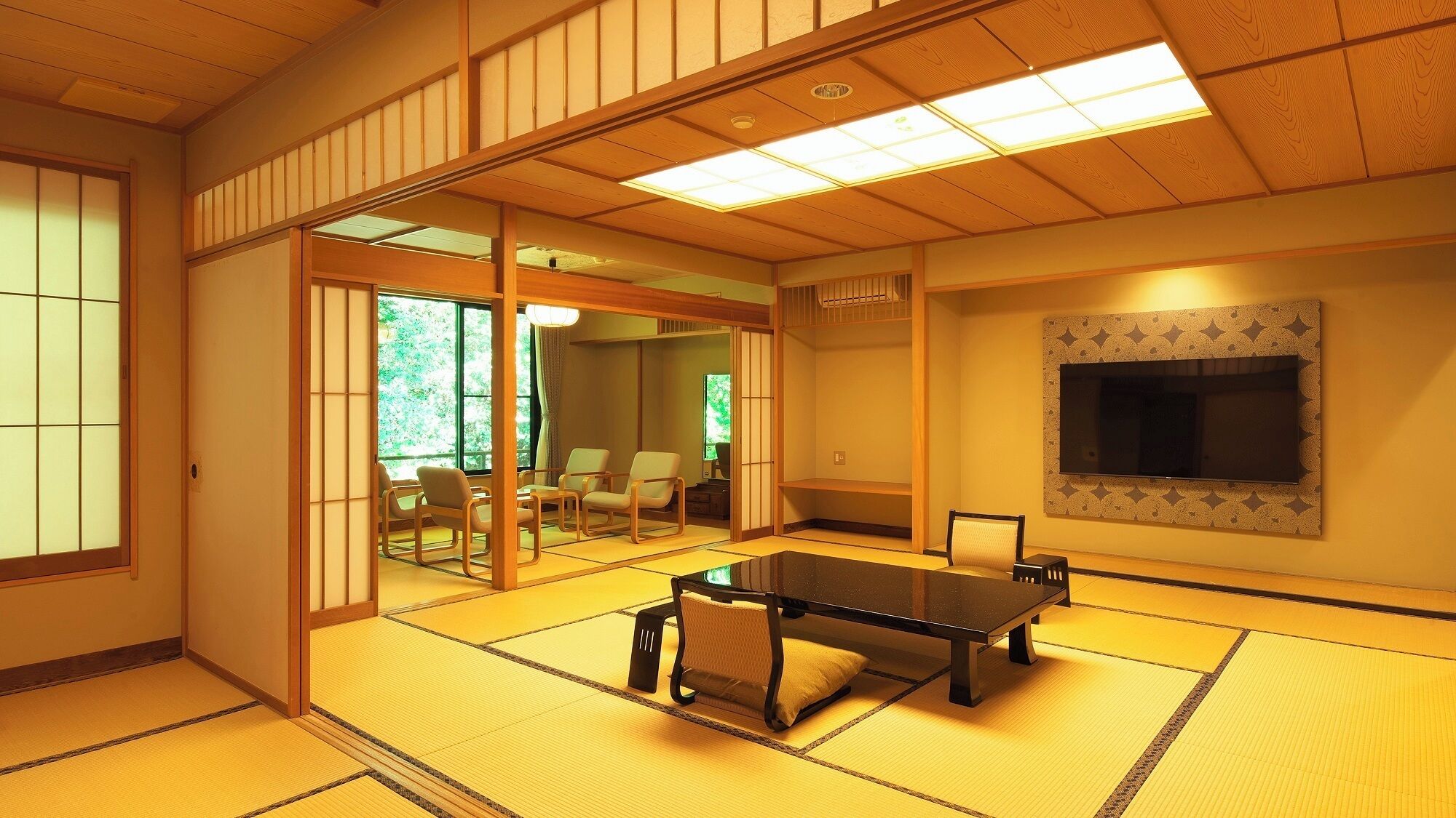 A tatami mat room with a tatami mat table, sliding doors, a television, and a view of a garden.