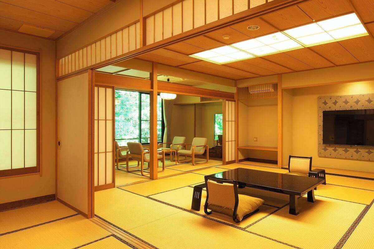 Una habitación con esteras de tatami, una mesa de tatami, puertas correderas, un televisor y vistas a un jardín.
