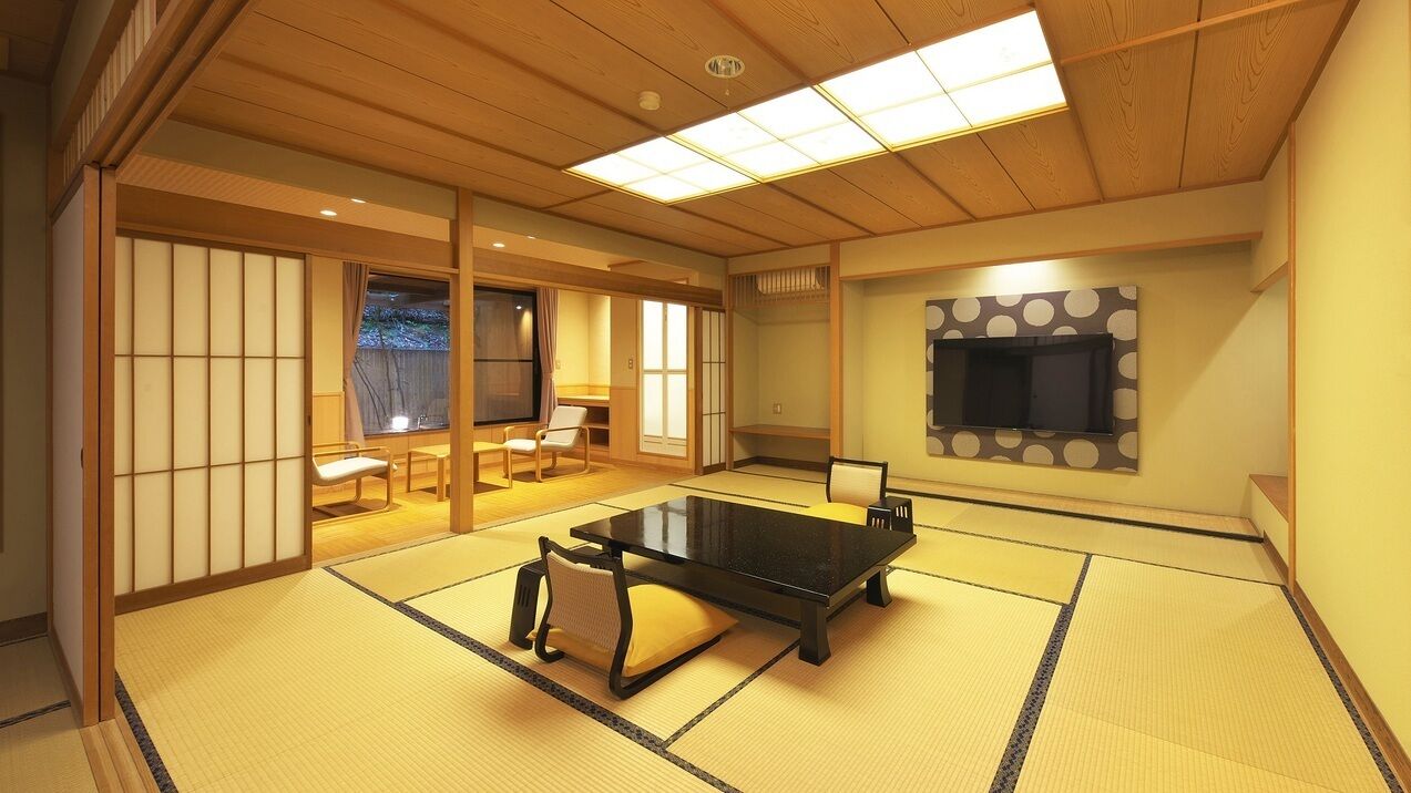 A tatami mat room with a low table, chairs, a TV, and sliding doors.