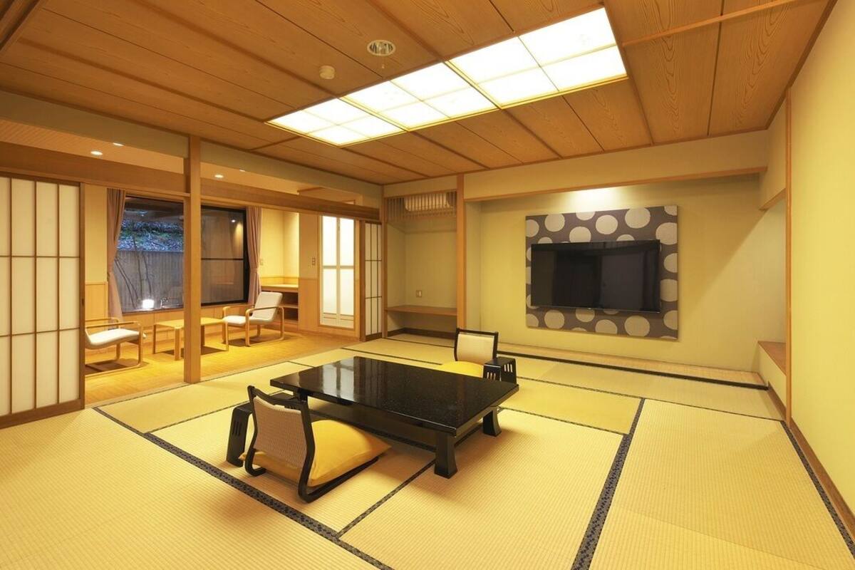 Una habitación con tatamis, una mesa baja, sillas, un televisor y puertas correderas.