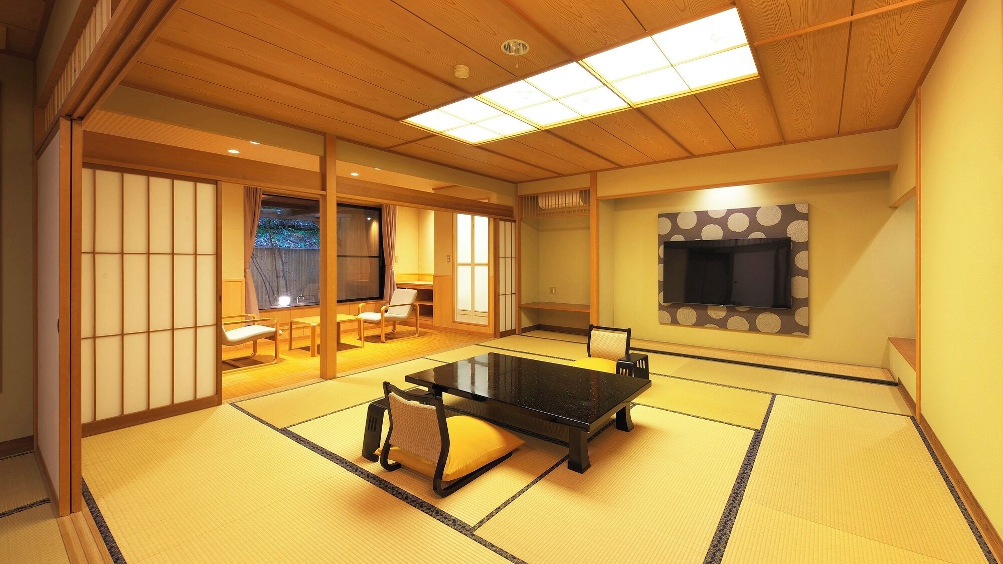 A tatami mat room with a tatami mat table, chairs, a television, and sliding doors.
