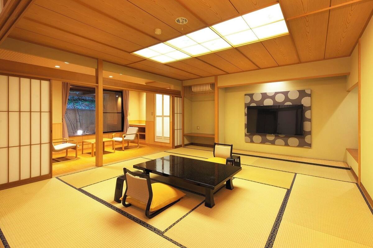 Una habitación con suelo de tatami, una mesa de tatami, sillas, un televisor y puertas correderas.