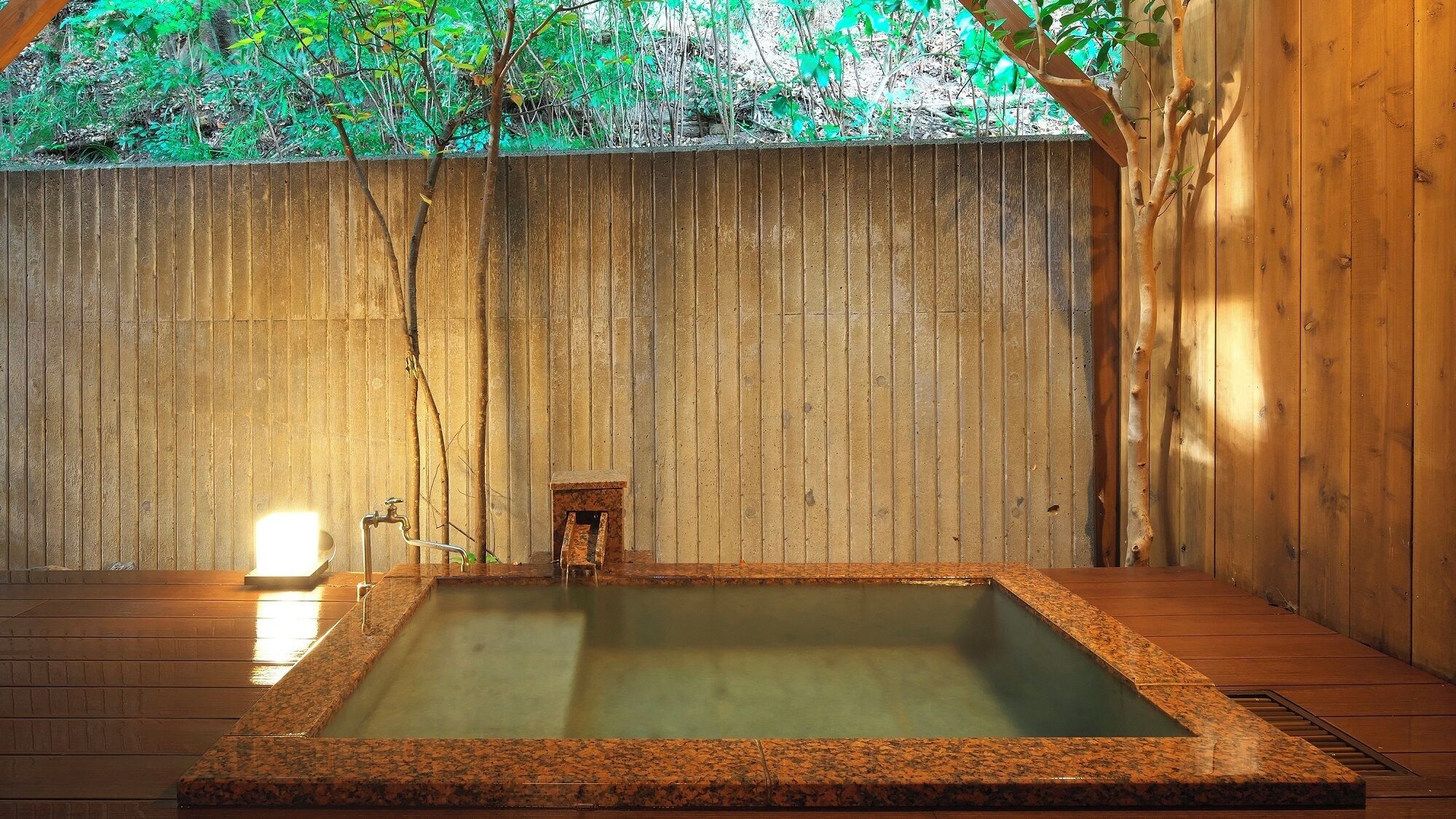 A hot spring bath area with a wooden deck, a small wooden structure, and a wooden wall.