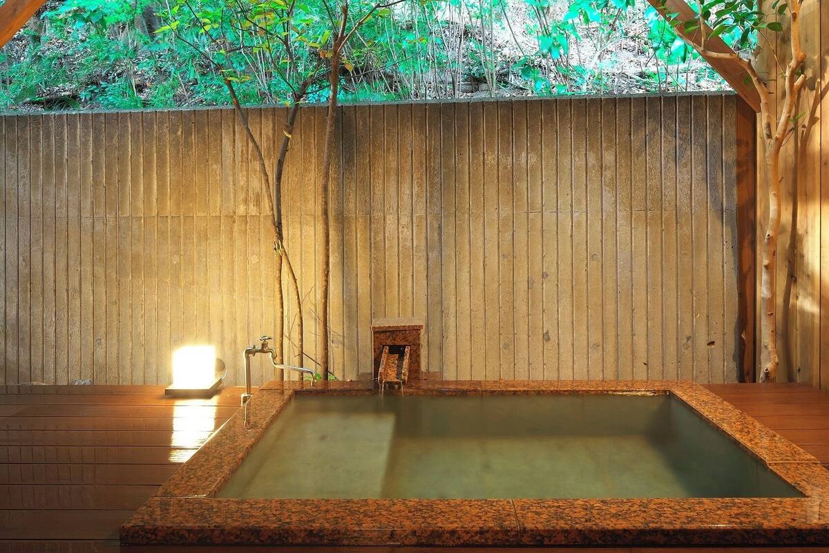 Zona de baños termales con una terraza de madera, una pequeña estructura de madera y un muro de madera.