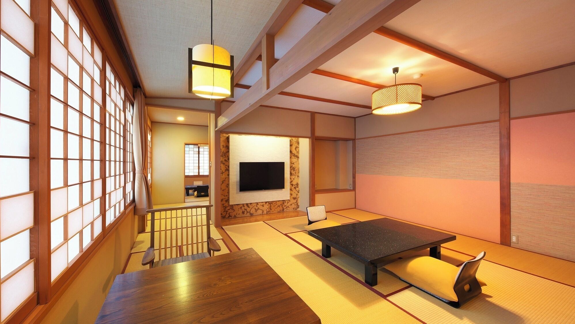 A traditional Japanese room with tatami flooring, a low table, a TV mounted on the wall, and sliding doors.