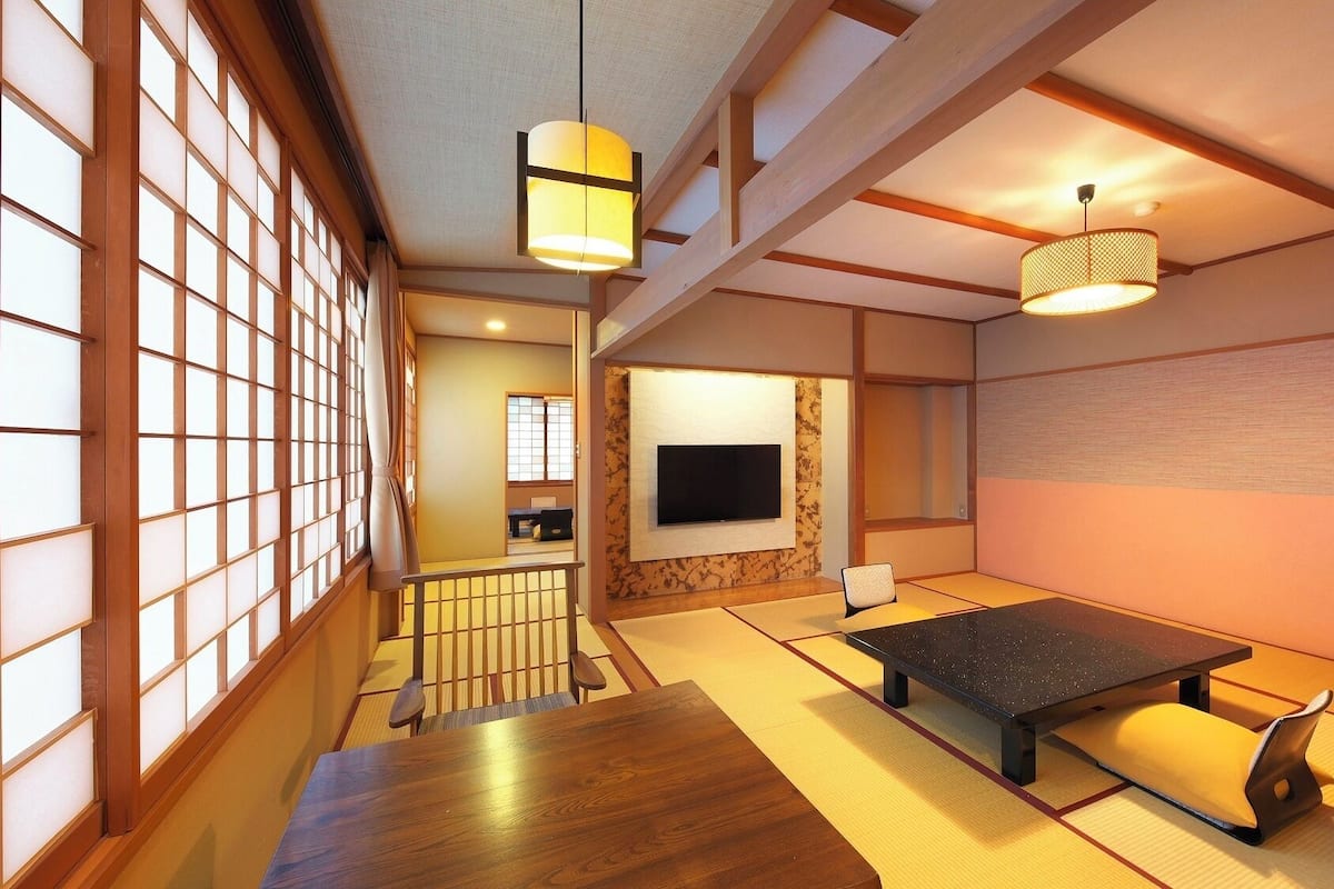 Una habitación japonesa tradicional con suelo de tatami, una mesa baja, un televisor montado en la pared y puertas correderas.