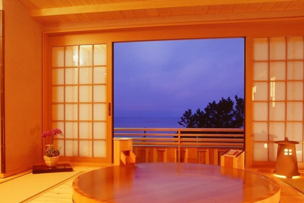 A traditional Japanese room with tatami flooring, a tatami mat table, a low wooden bench, a shoji screen, and a view of the sea.