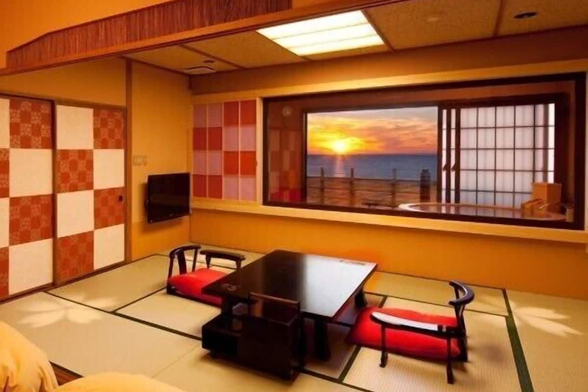 A traditional Japanese-style room with tatami flooring, a low table, and a view of the sunset through a large window.