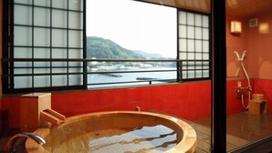 A traditional Japanese onsen with a wooden bathtub, a view of a mountainous landscape, and red tiled walls. - Toi Onsen Suishoutei (Izu)
