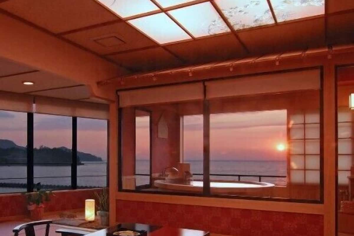 A dining area with a table and chairs, large windows with a view of the sunset, and a wooden ceiling.