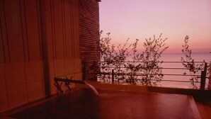 A balcony with a view of the sea, a wooden building, and a metal railing. - Toi Onsen Suishoutei (Izu)