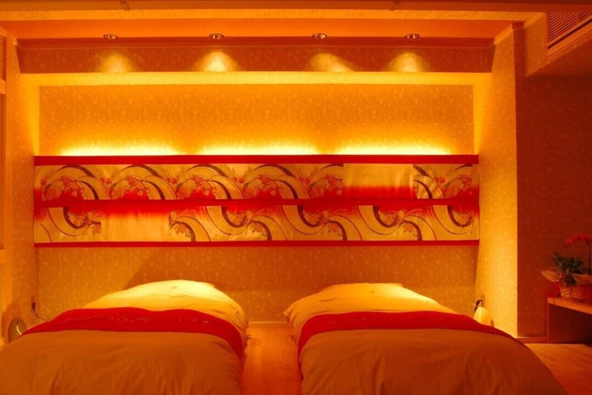 A room with two beds, a decorative headboard, and a small table with a vase.