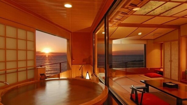 A room with a large window, a round wooden table, and a seating area with red cushions. - Toi Onsen Suishoutei (Izu)