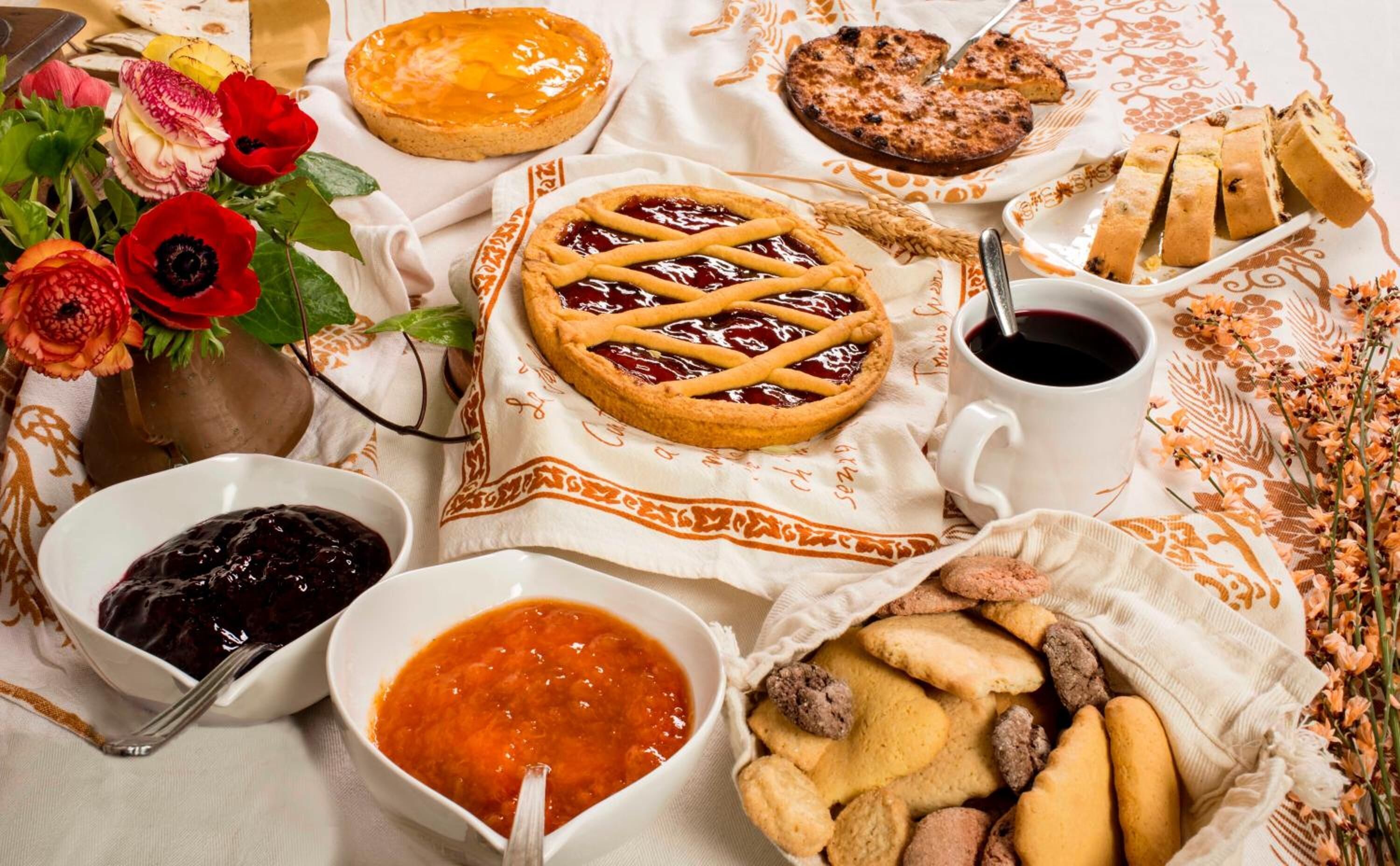 A table set with various baked goods, including pies, bread, and cookies, along with bowls of jam and a cup of tea.