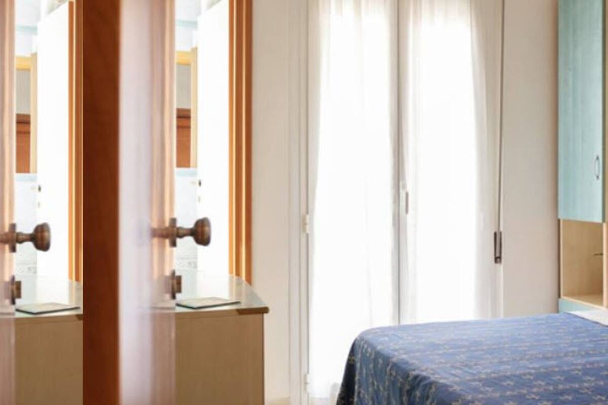 A bedroom with a bed, a nightstand, a window with curtains, and a door.