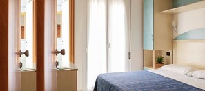 A bedroom with a bed, a nightstand, a window with curtains, and a door. - Hotel Kadett (Rimini)