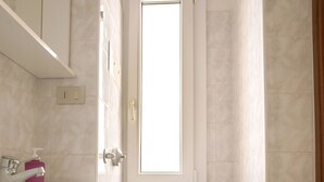 Une salle de bain avec un lavabo blanc, des toilettes et une fenêtre.