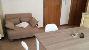 Un salon avec un canapé beige, une chaise blanche et une table à manger en bois.